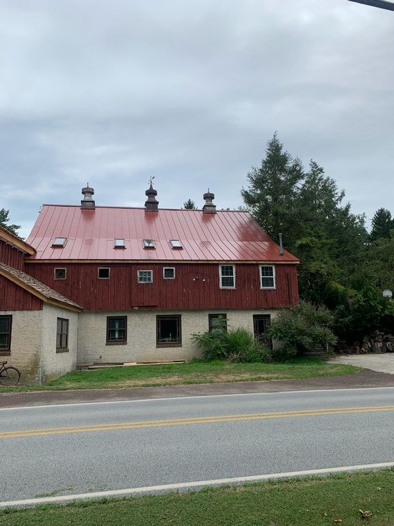 A red barn with a metal roof is next to a road.