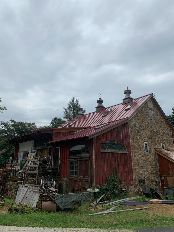 A red barn with a metal roof is sitting in the middle of a grassy field.