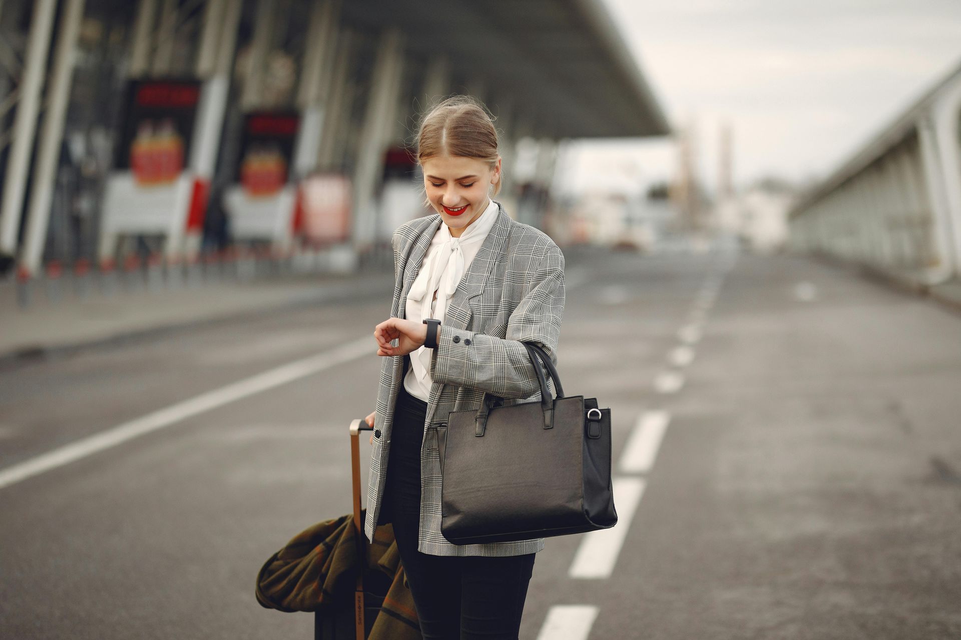 A woman is walking down the street with a suitcase and looking at her watch.