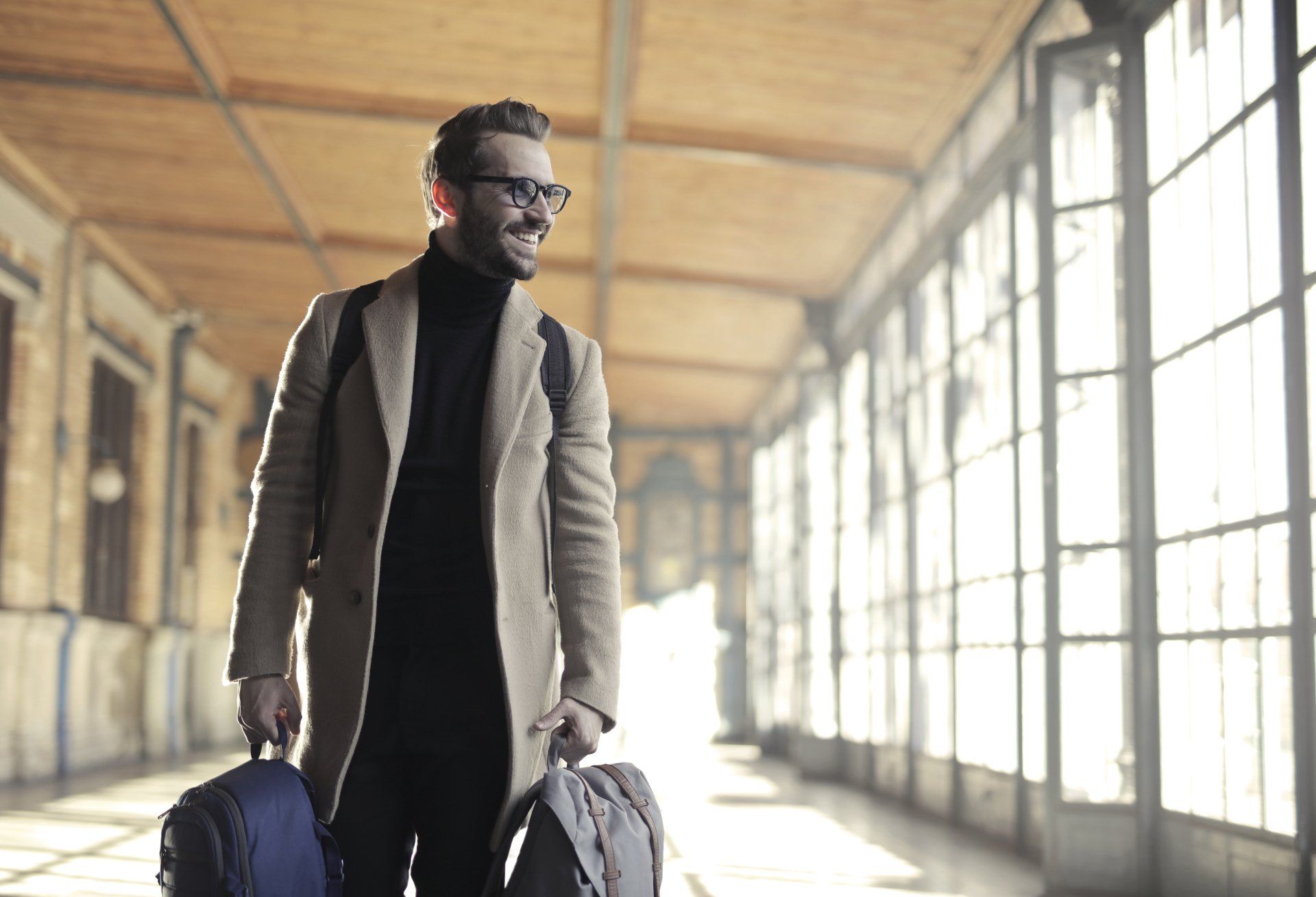A man is walking down a hallway with two suitcases.