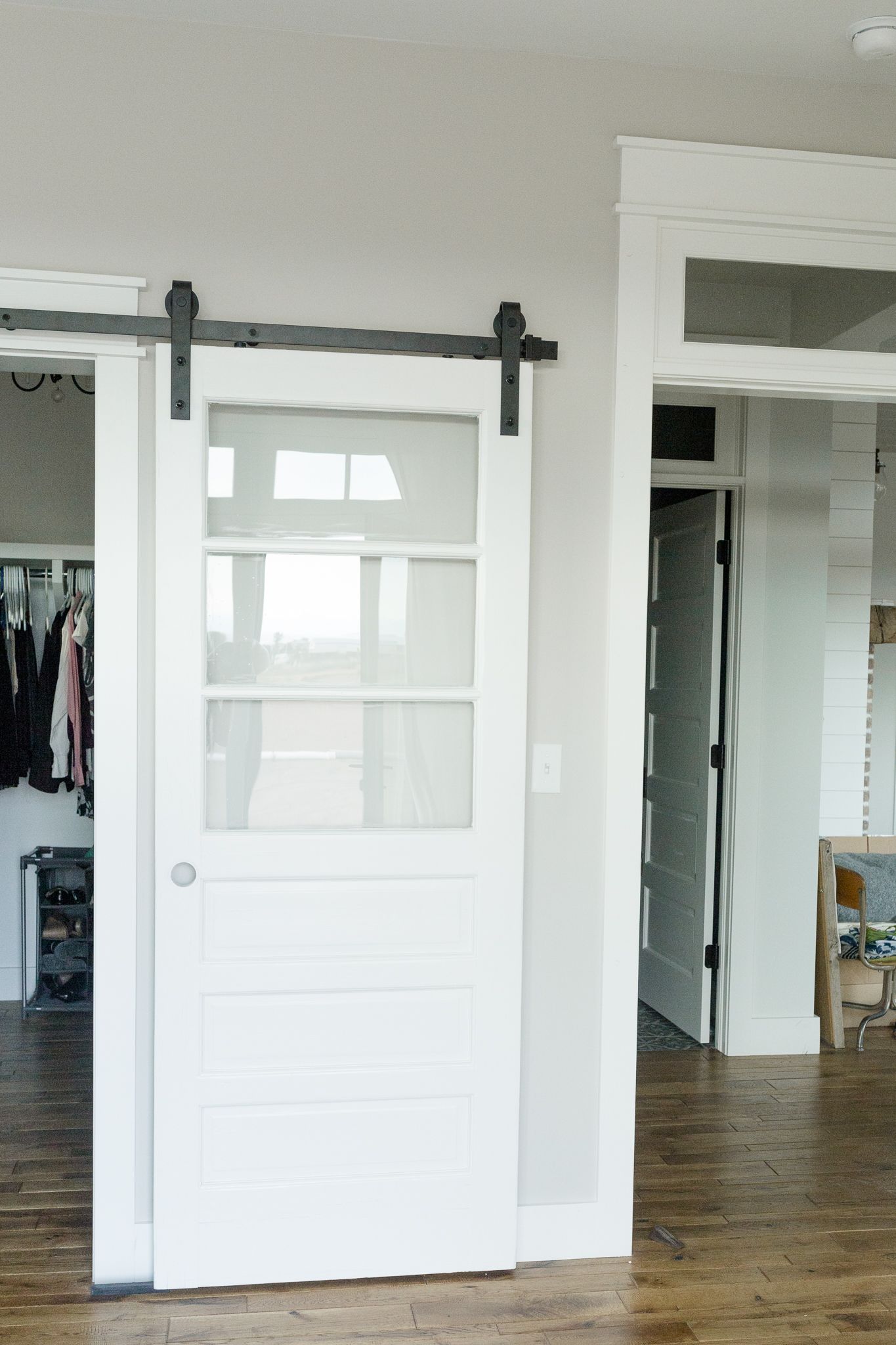 White barn door with black hardware, open to a closet and an adjacent room.