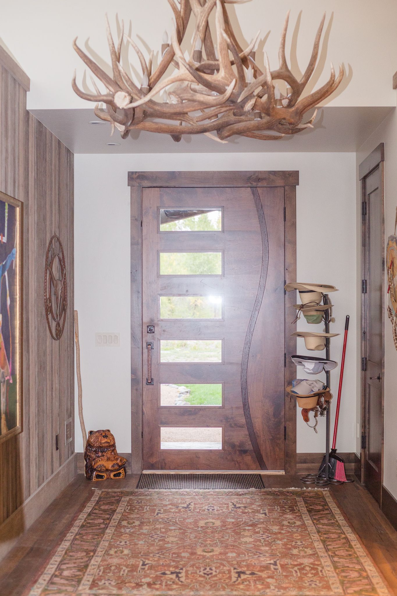 Entryway with wooden door, antler chandelier, and patterned rug.