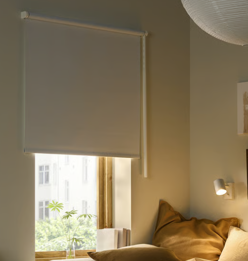 Dormitorio con cama, cortinas romanas grises y una silla con vista a un verde paisaje exterior.