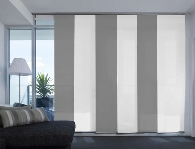 Persianas que cubren una puerta corrediza de vidrio. Paneles verticales alternados en gris y blanco.