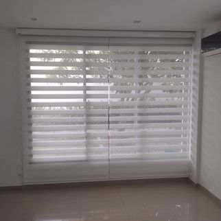 Tres persianas blancas de cebra en las ventanas de una habitación moderna; la luz del sol entra a través de ellas.