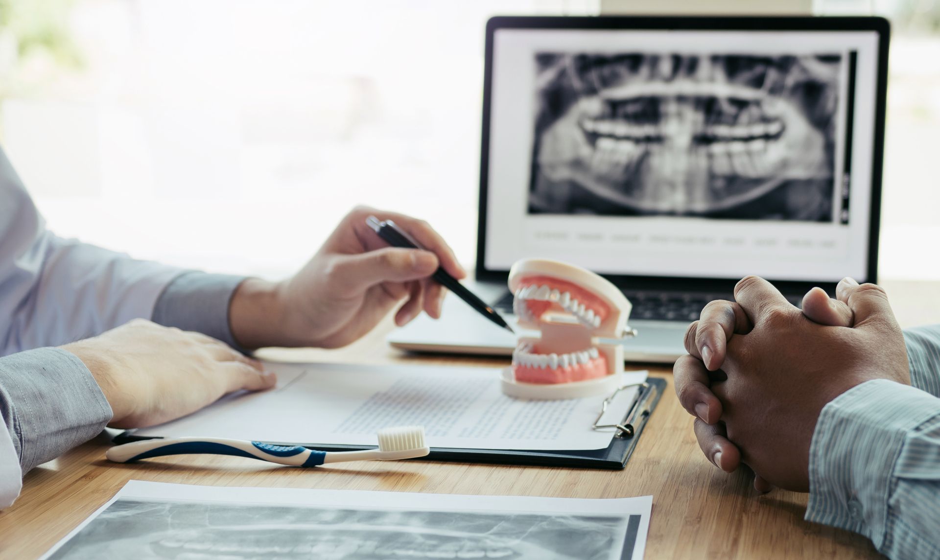 Dentist pointing at a jaw model while showing X-ray on laptop to a patient.