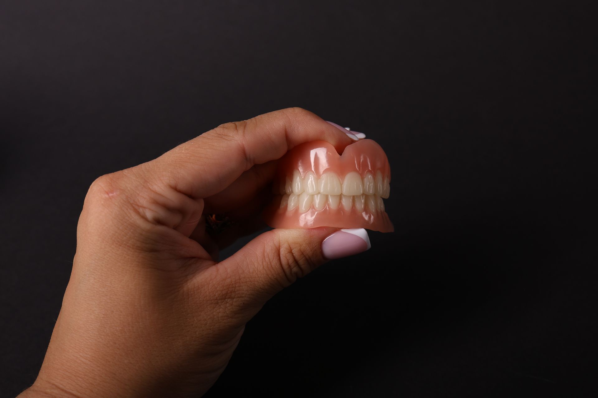 Hand holding a set of dentures against a dark background.