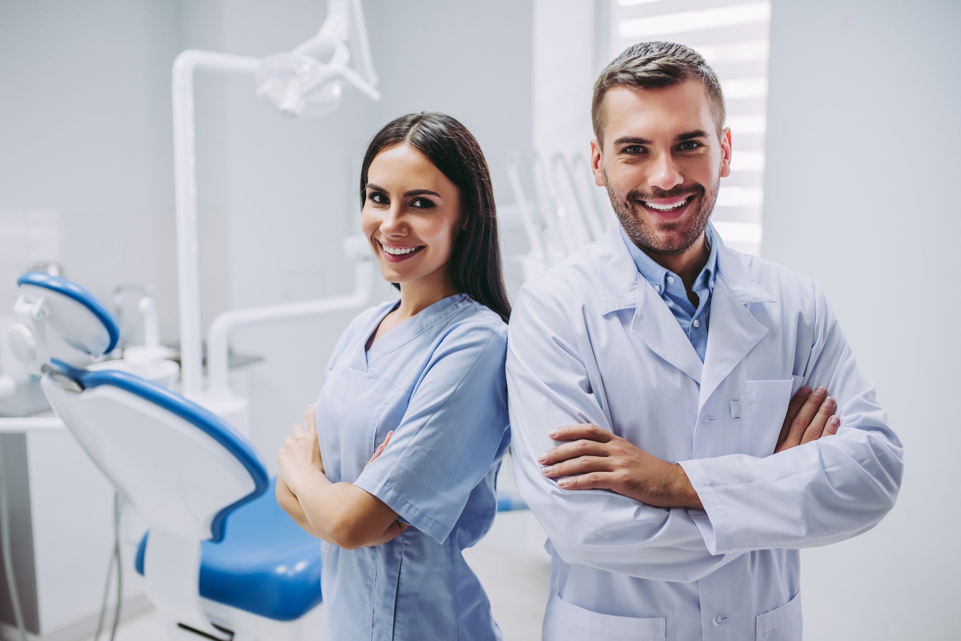 Dentist and assistant smiling, arms crossed, in a bright dental office.