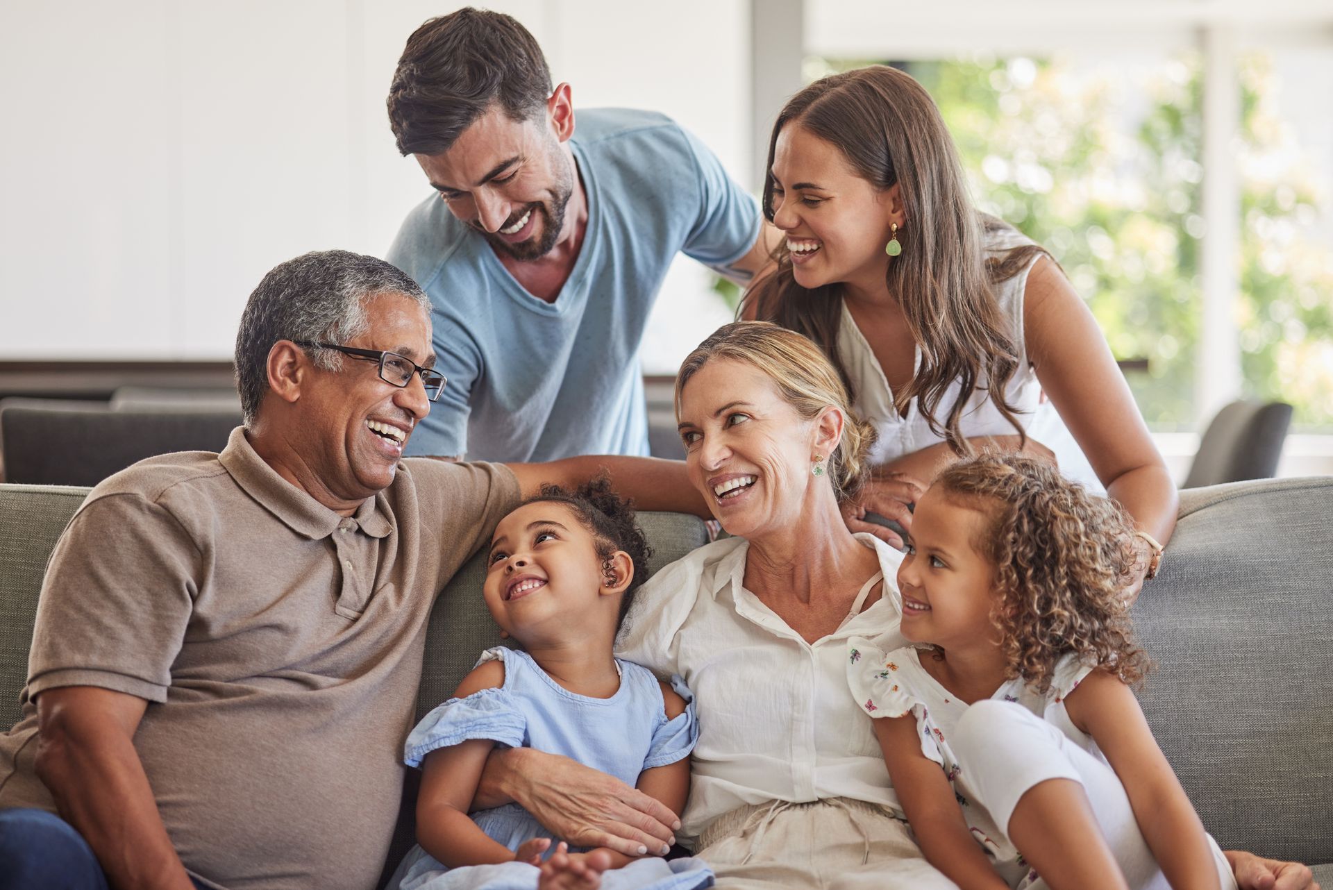 Multigenerational family, laughing together on a couch in a bright living room.