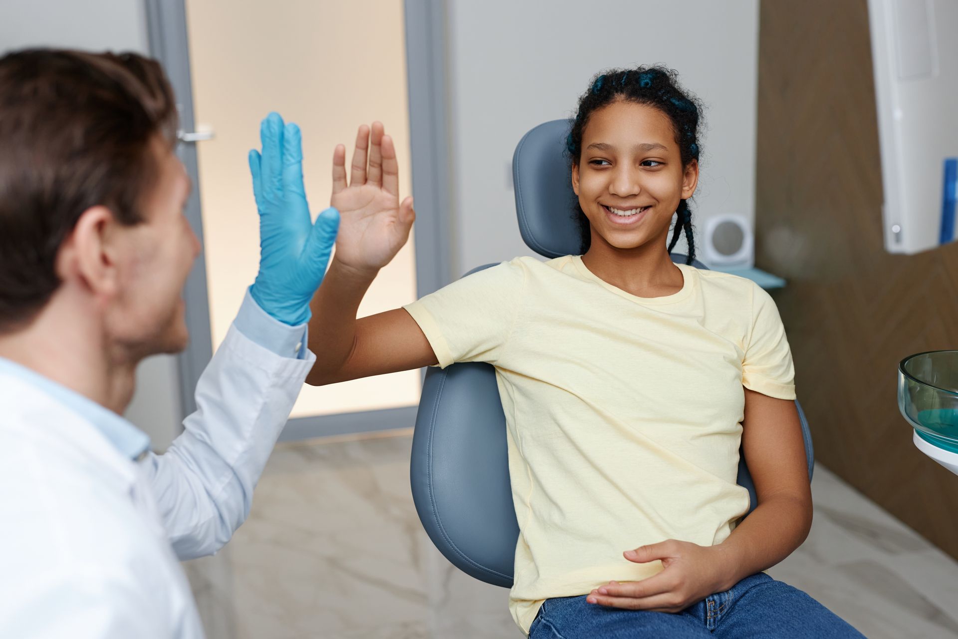 Dentist giving a high five to a smiling patient after a check-up in a dental office.