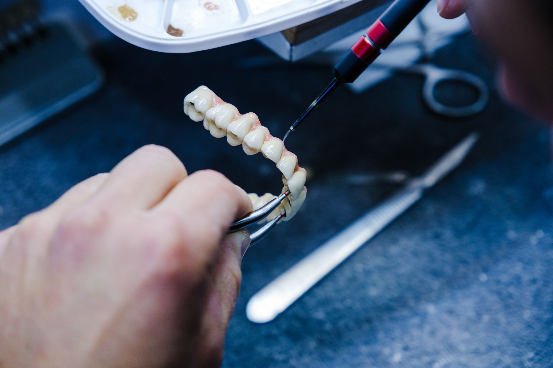 A dental technician working on a set of artificial teeth with tools and a bright light in a lab setting.