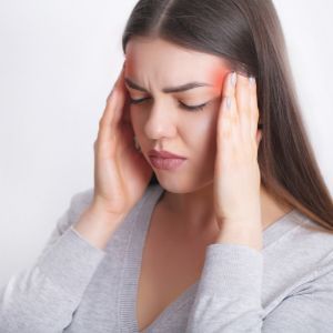 a woman is holding her head in pain because of a headache .