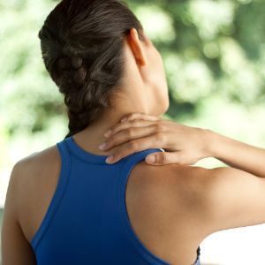 a woman in a blue tank top is holding her neck in pain