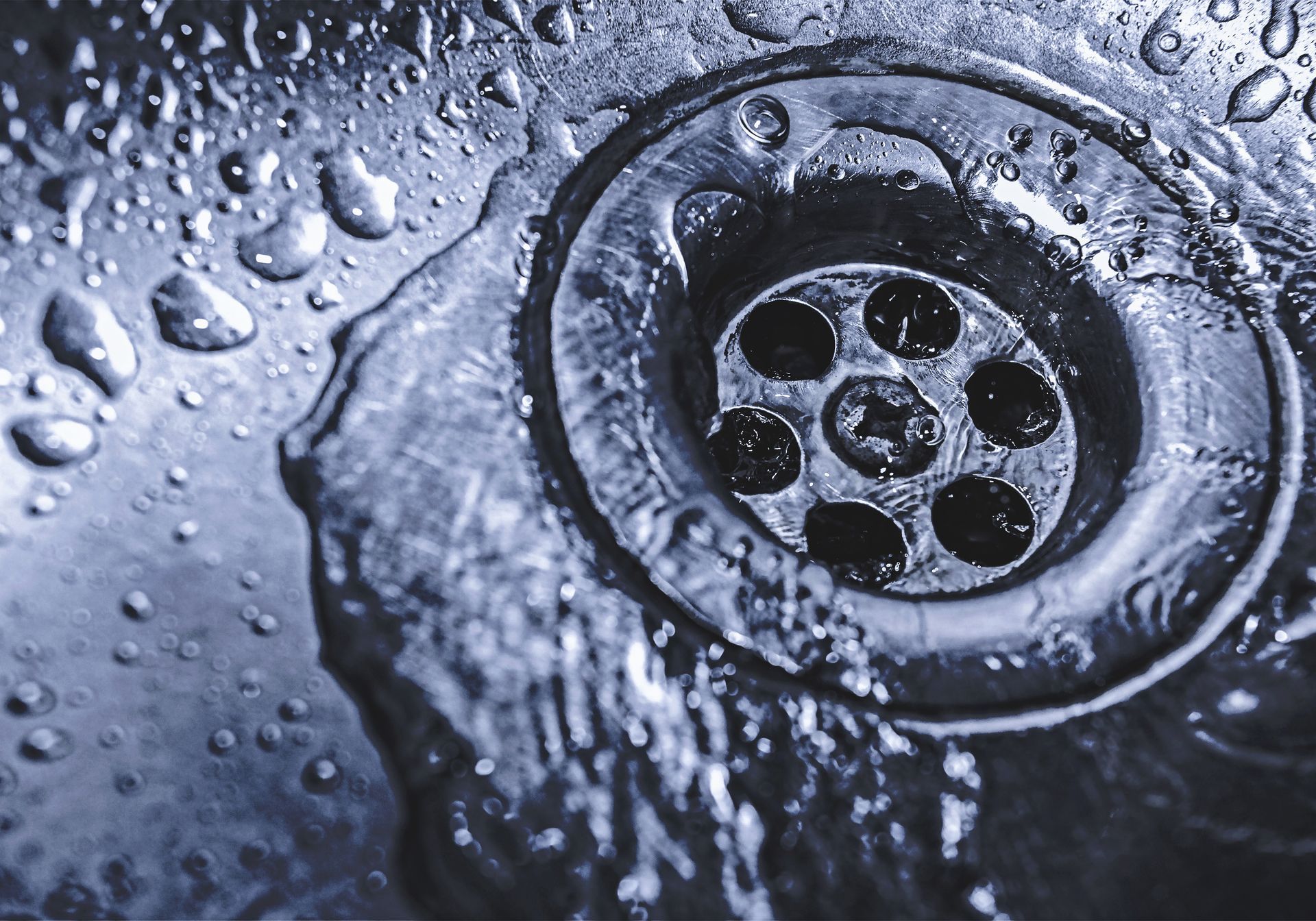 Close-up of water droplets flowing into a metal sink drain.