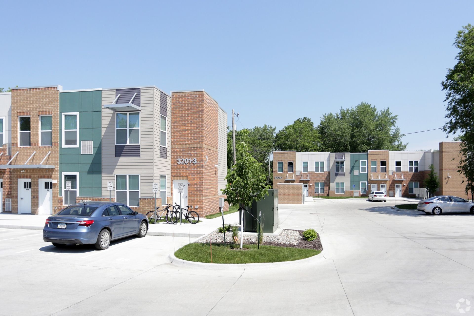 A blue car is parked in front of a row of apartment buildings