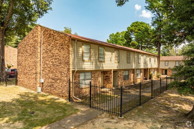 A brick apartment building with a fence around it and trees in the background.