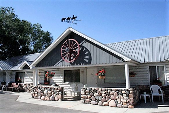A rustic single-story lodge with a wagon wheel wall ornament, stone porch base, and a horse weather vane on the roof.