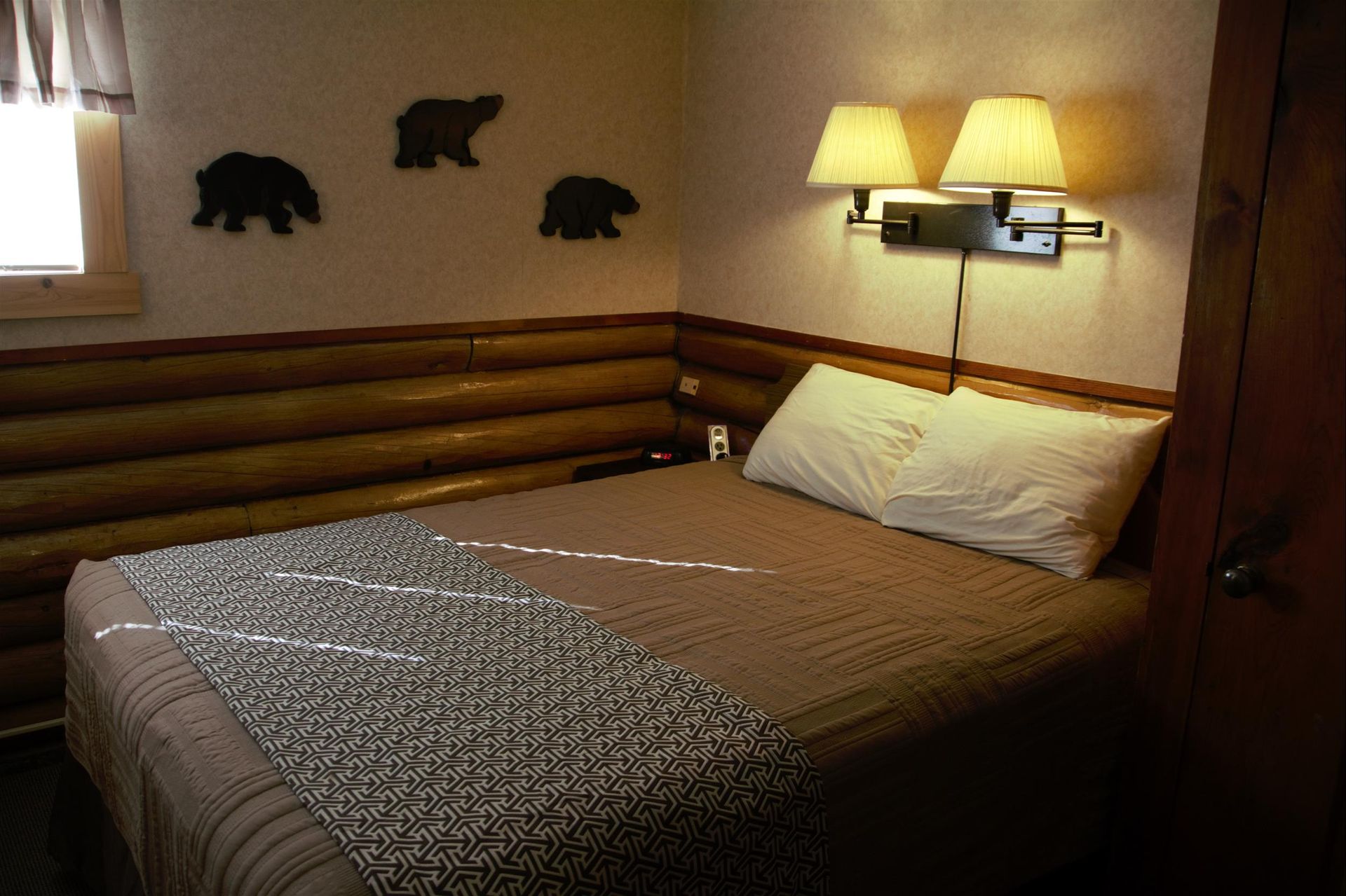 A rustic bedroom with a bed featuring a patterned throw blanket, log walls, bear decor, and wall-mounted lamps.