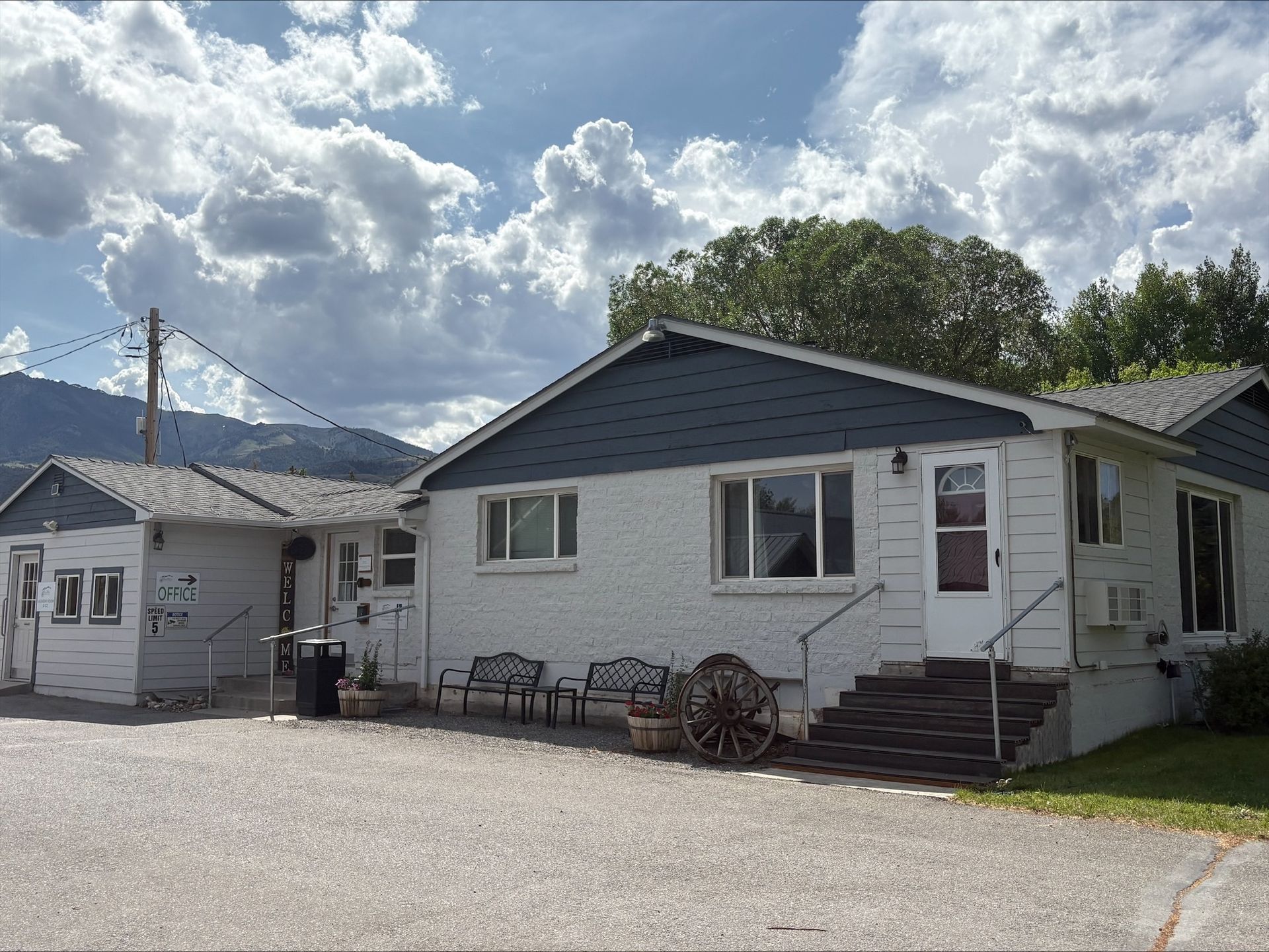 Single-story building with white brick walls, dark blue trim, a gravel parking area, and a metal roof under a cloudy sky.