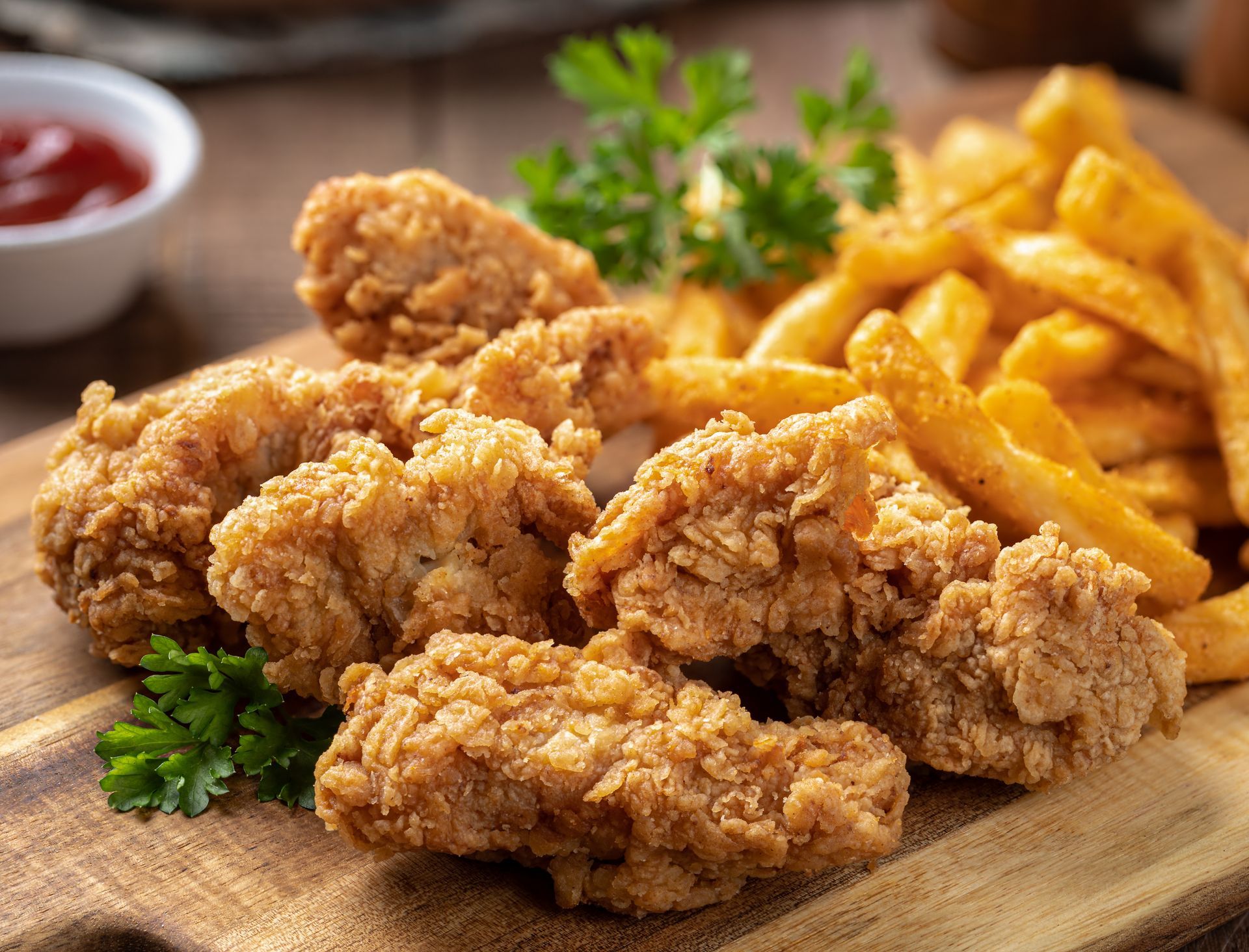 Crispy fried chicken bites served with golden french fries and a small bowl of dipping sauce on a wooden board.