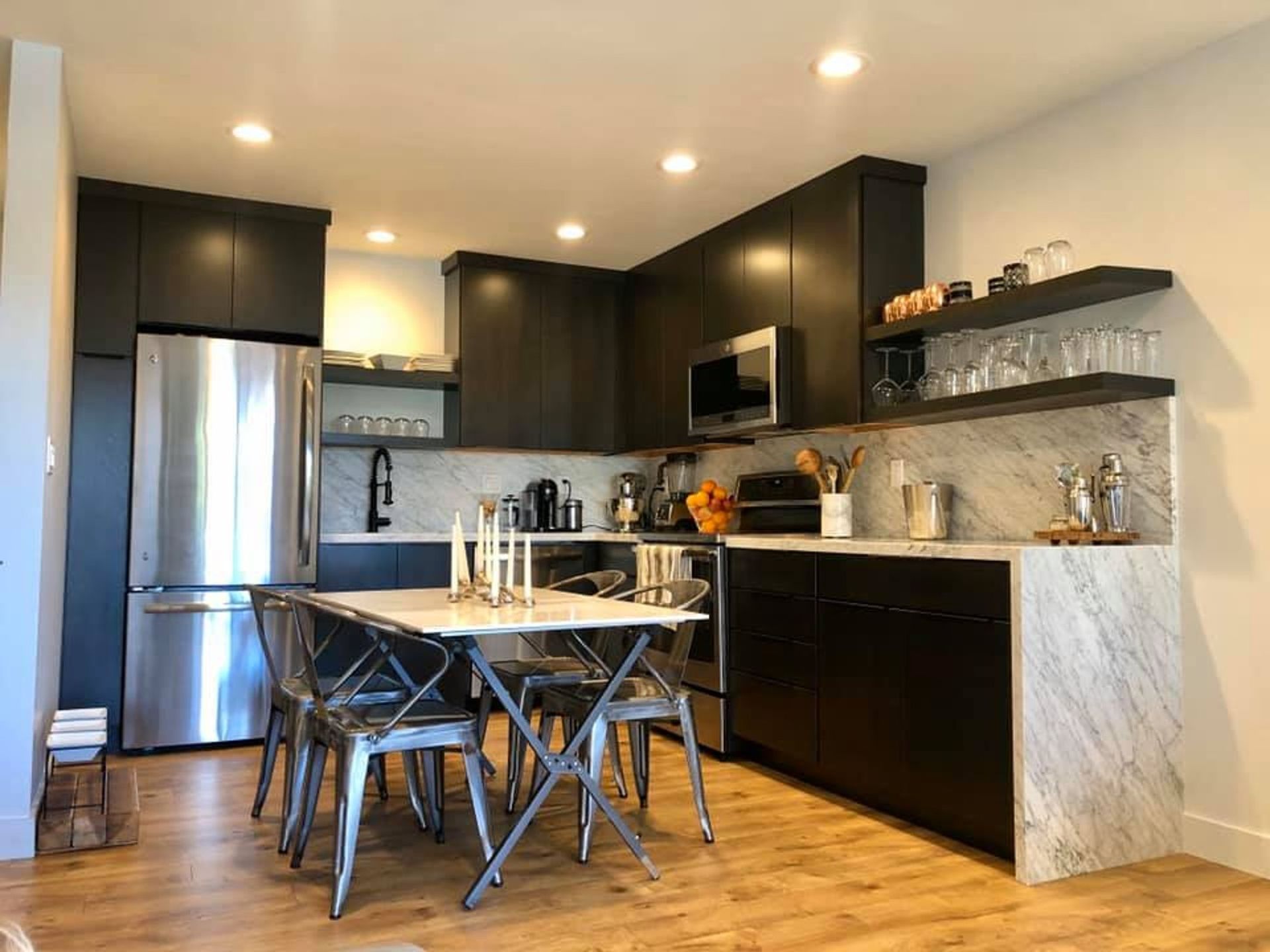 A kitchen with black cabinets , stainless steel appliances , a table and chairs.