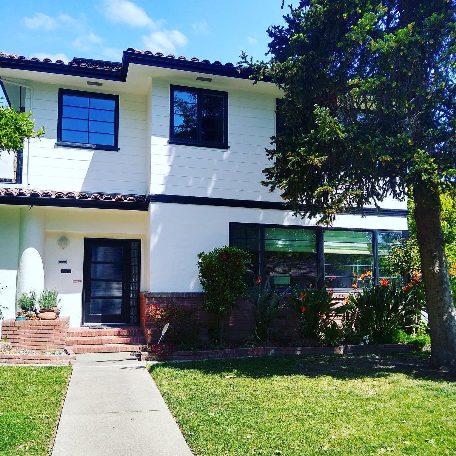 A white house with black trim and a tree in front of it