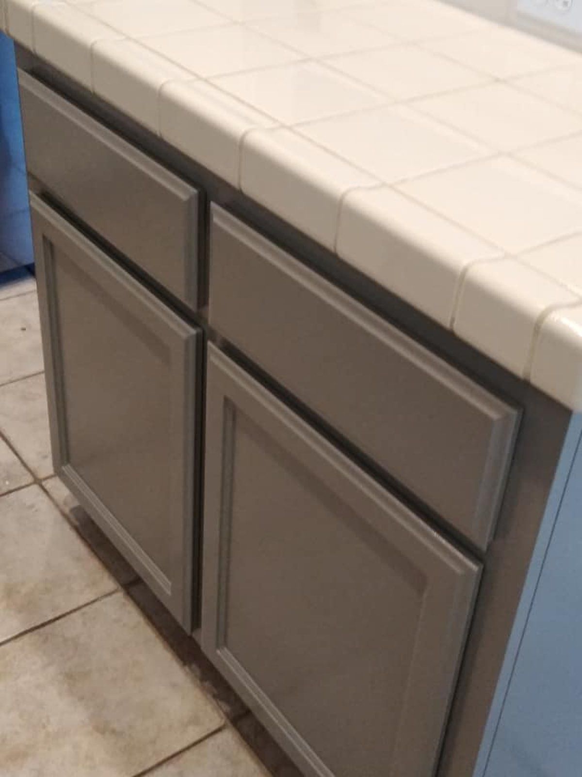A kitchen counter with gray cabinets and a white counter top.
