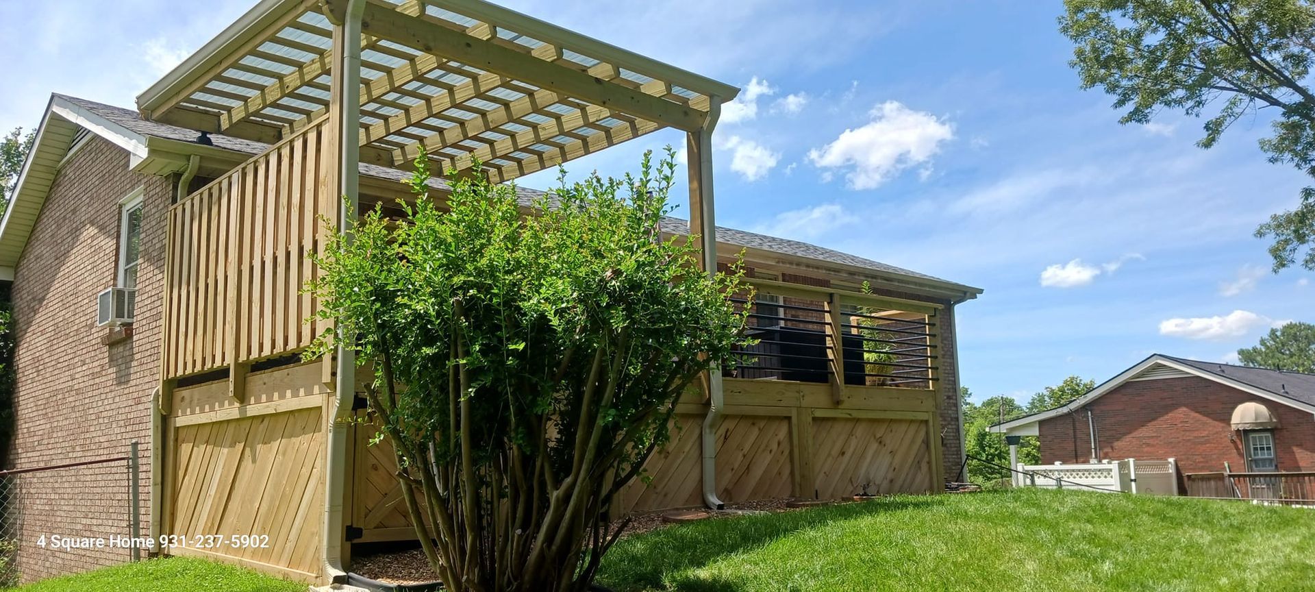Wooden deck with lattice panels and a pergola attached to a brick house, sunny day.
