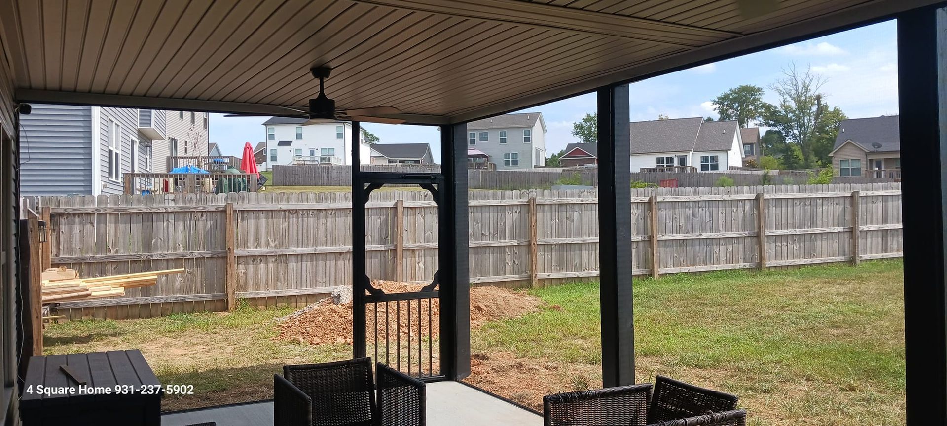 A screened porch overlooking a backyard with a wooden fence and houses in the background.