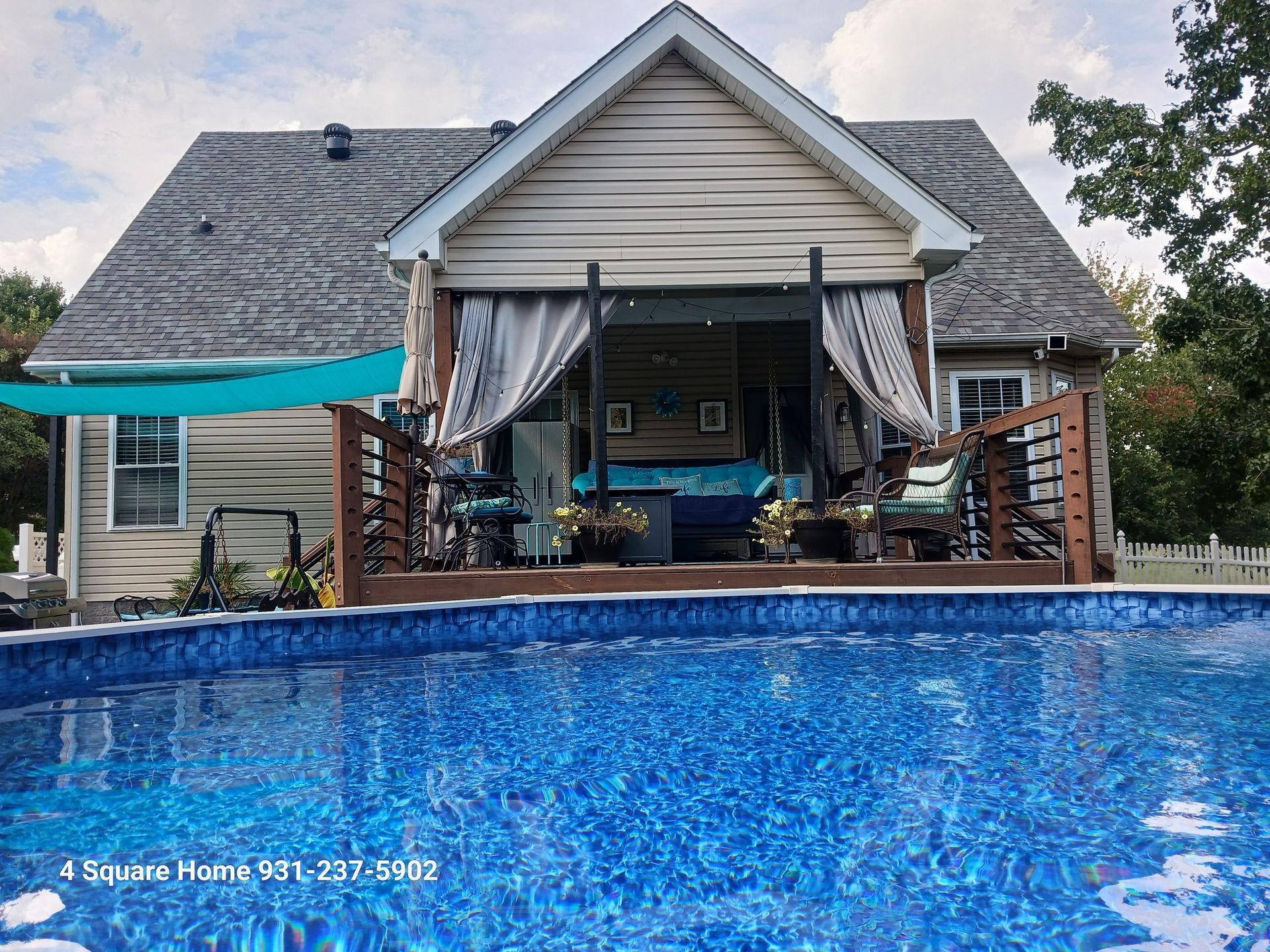 Pool with blue water in front of a house with a deck and curtains. Cloudy sky.