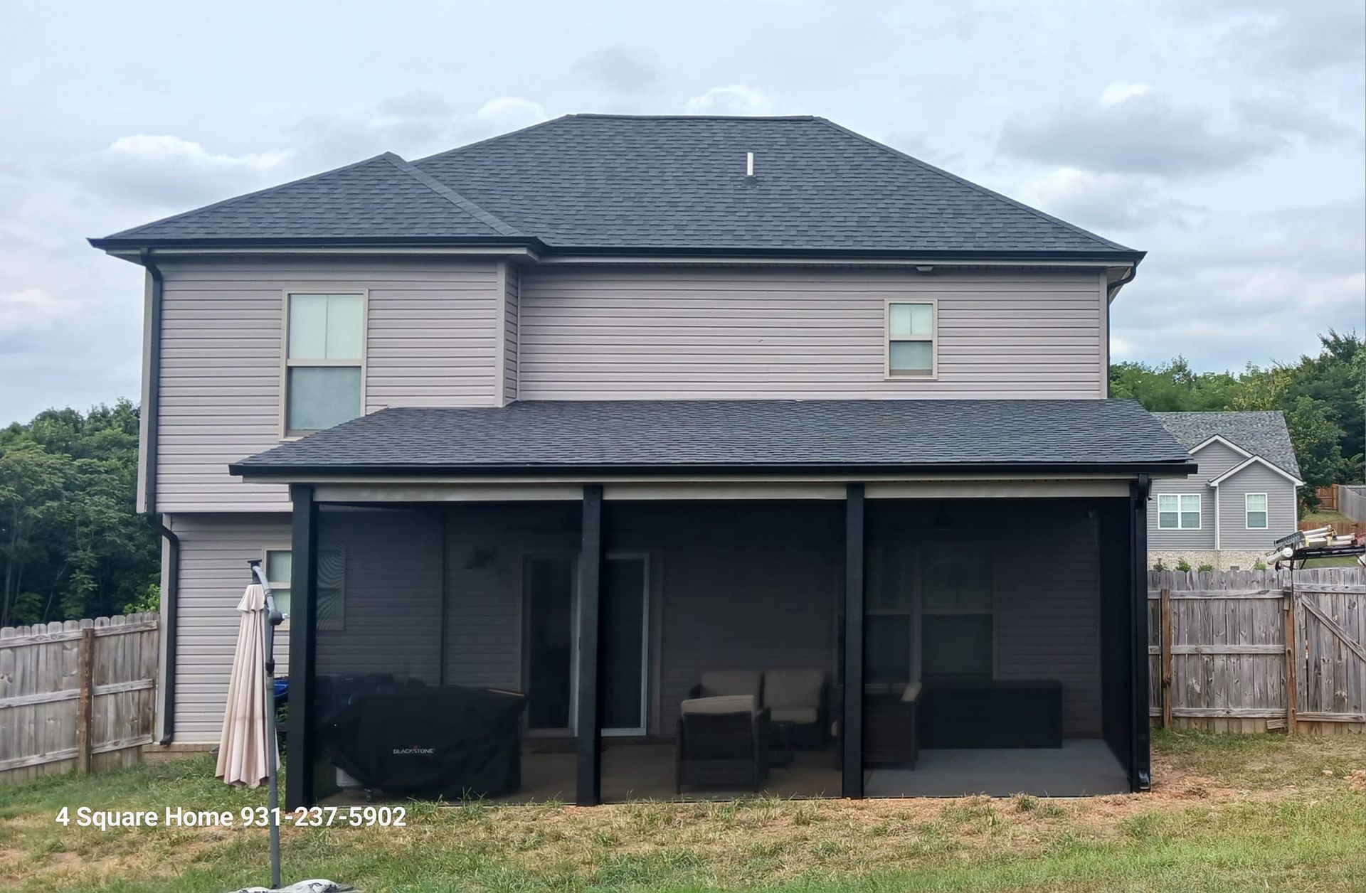 Back view of a house with a screened-in porch, gray siding and roof. The yard has a fence and grass.