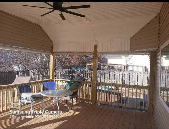 Covered wooden deck with a table, chairs, and a ceiling fan.