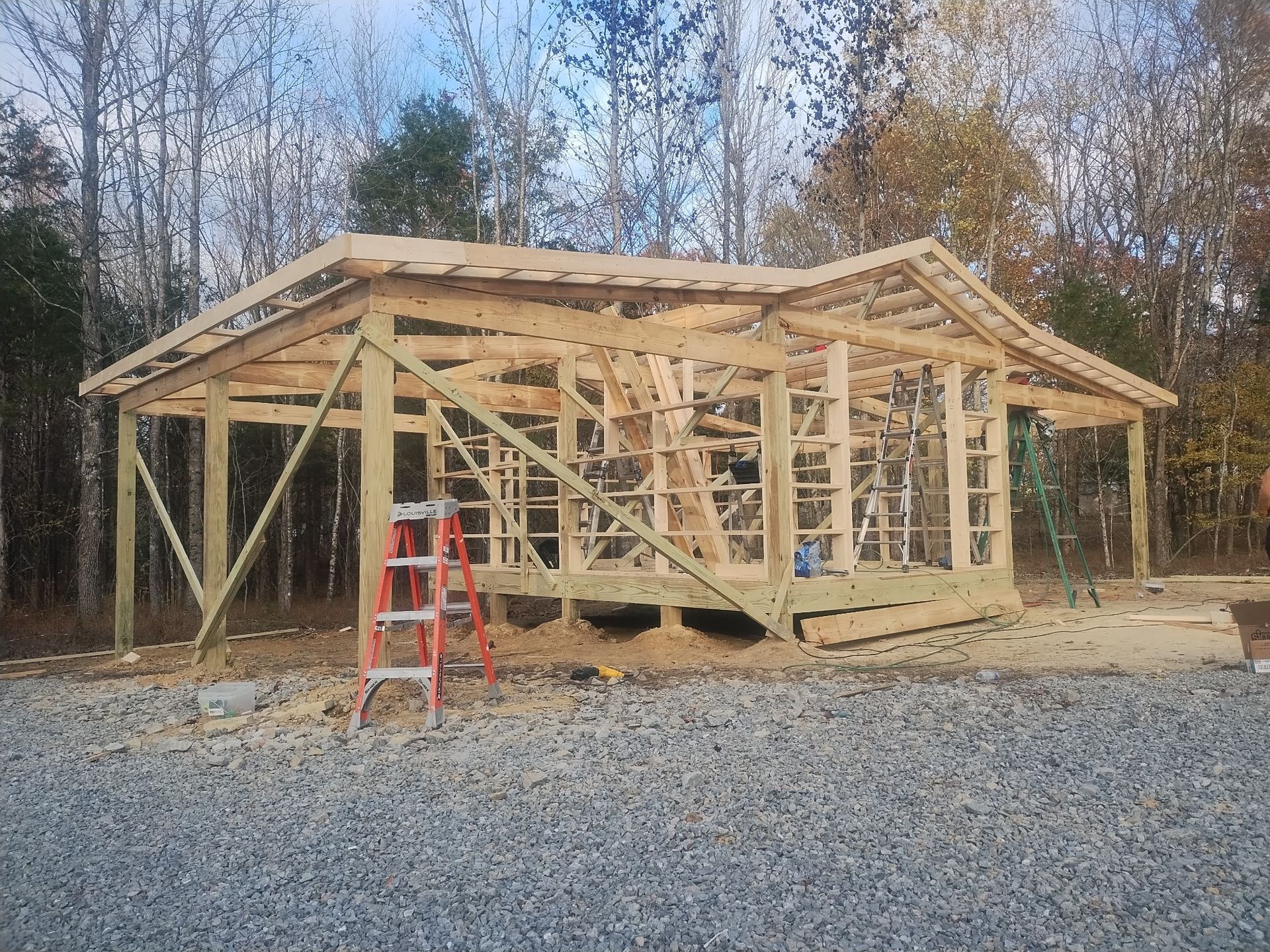 Wooden structure under construction outdoors with a ladder and gravel.