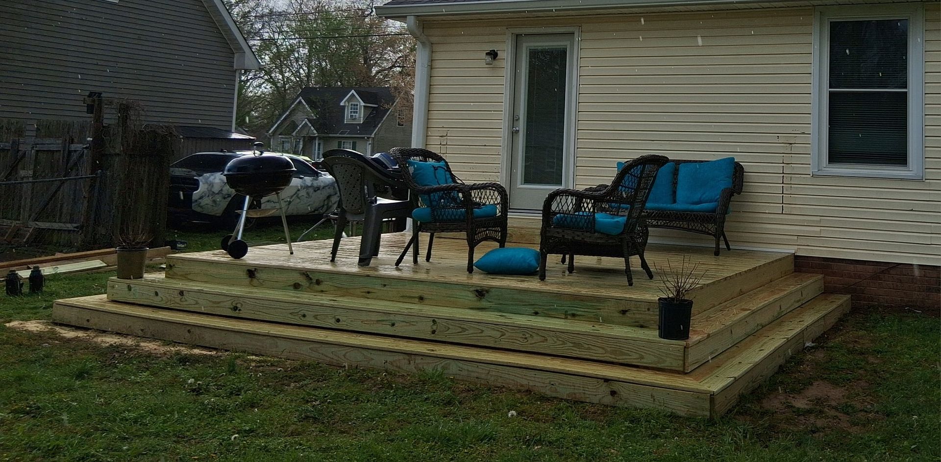 Newly built wooden deck with chairs and grill outside a house.