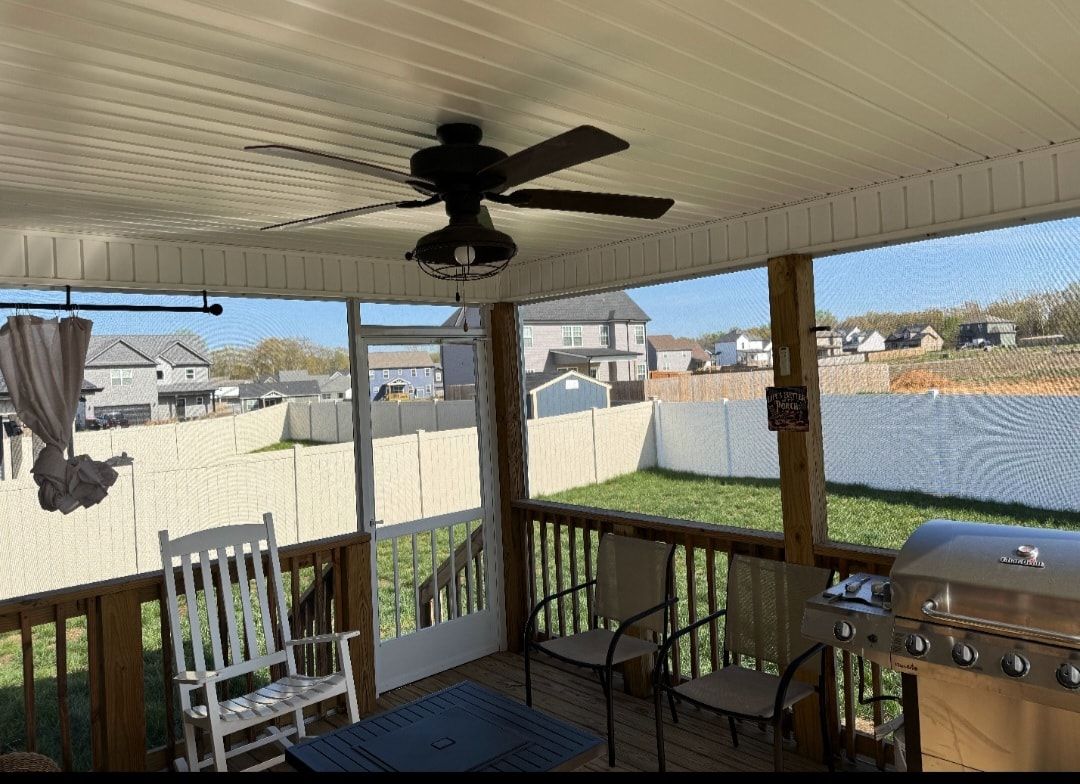 Screened-in porch with ceiling fan, overlooking a fenced backyard and neighboring houses.  Wooden deck, grill, chairs, rocking chair.