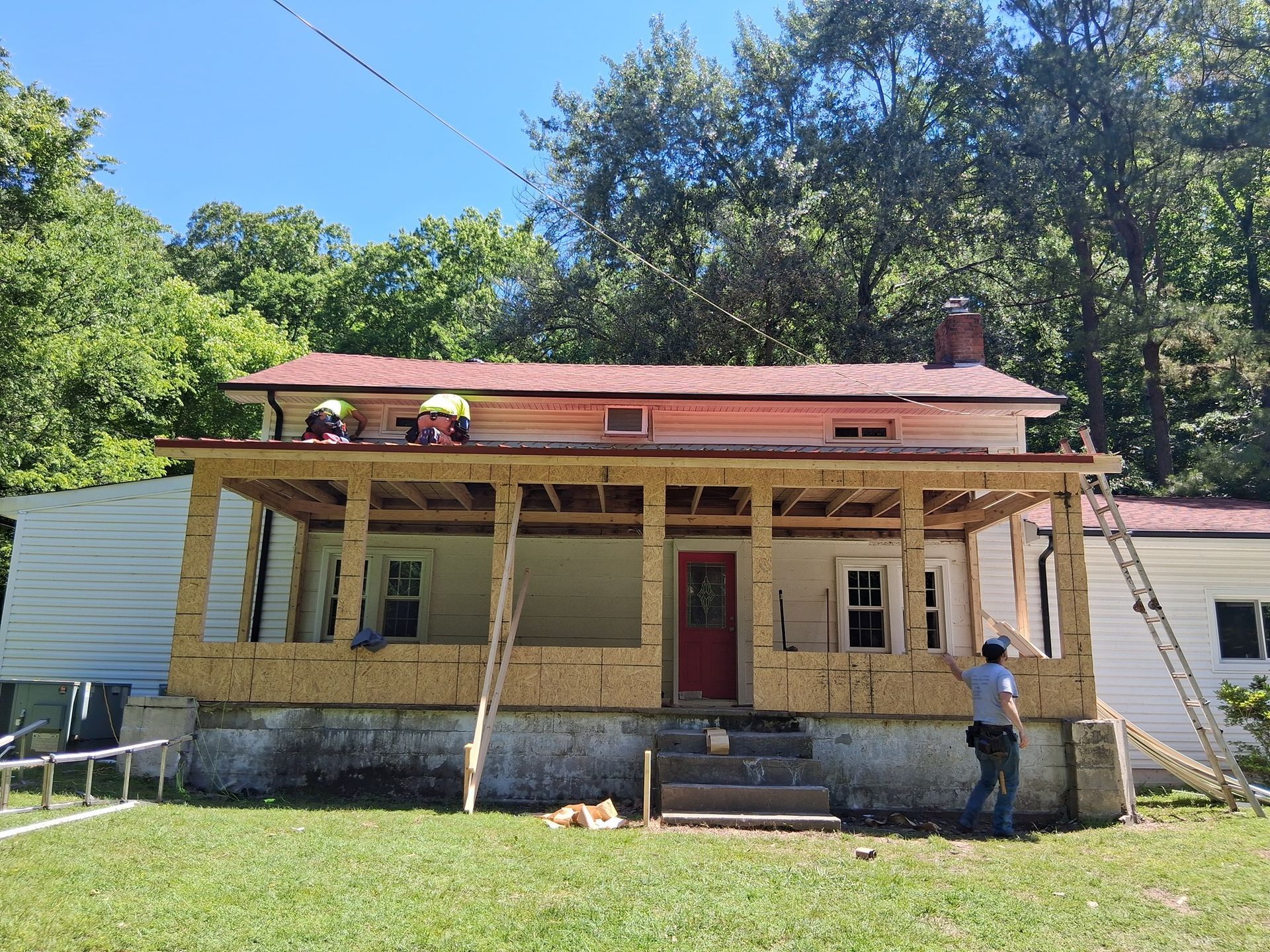 House under construction with exposed framing, red roof, and workers.