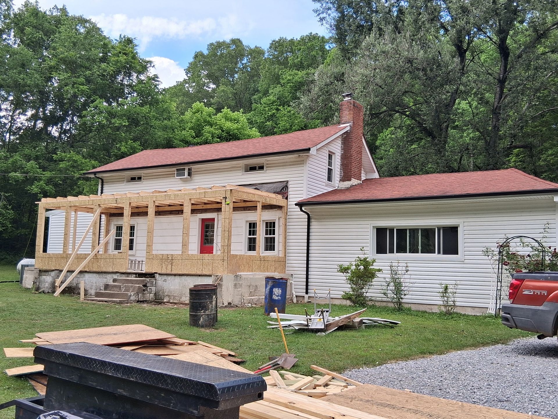 House under construction with a new porch frame, red door, red roof, and white siding.