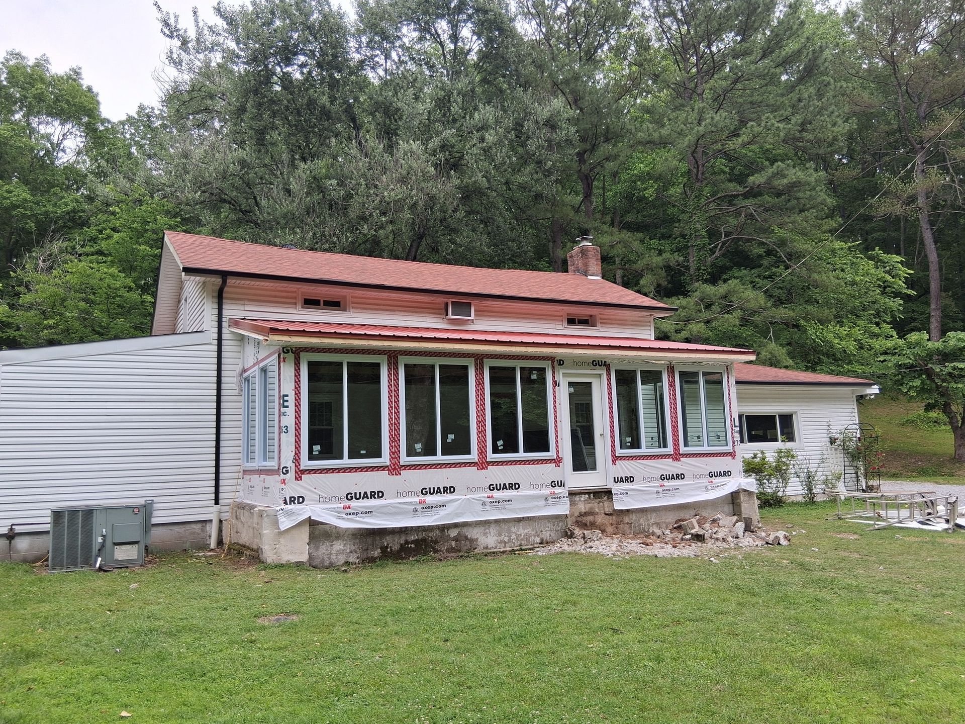 House under construction with exposed windows, new siding, and red roof, surrounded by trees.