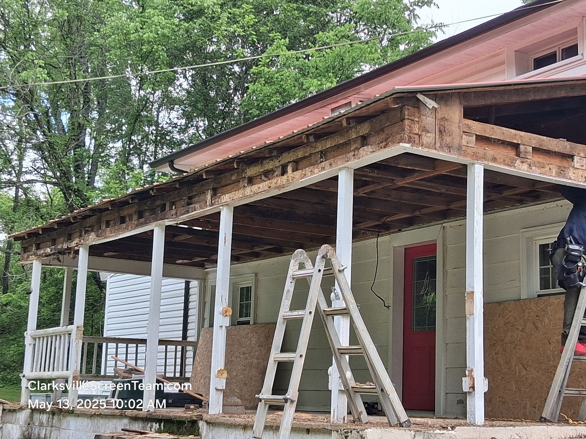 Porch renovation: Partially dismantled roof, white pillars, red door. Ladders present.