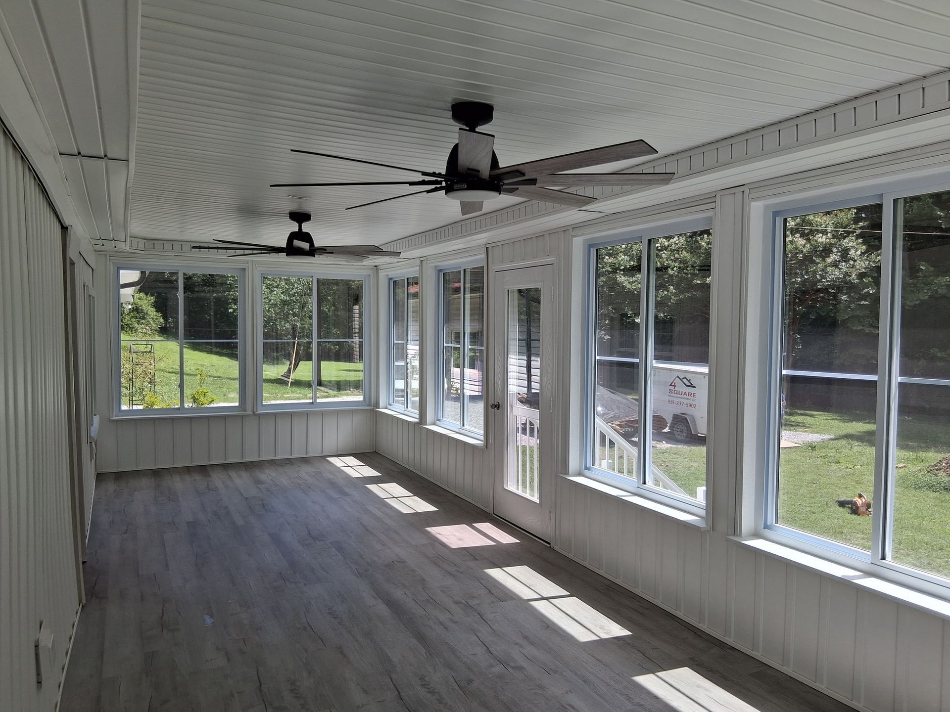 Sunroom with many windows, ceiling fans, and wood-look flooring overlooking a grassy backyard.