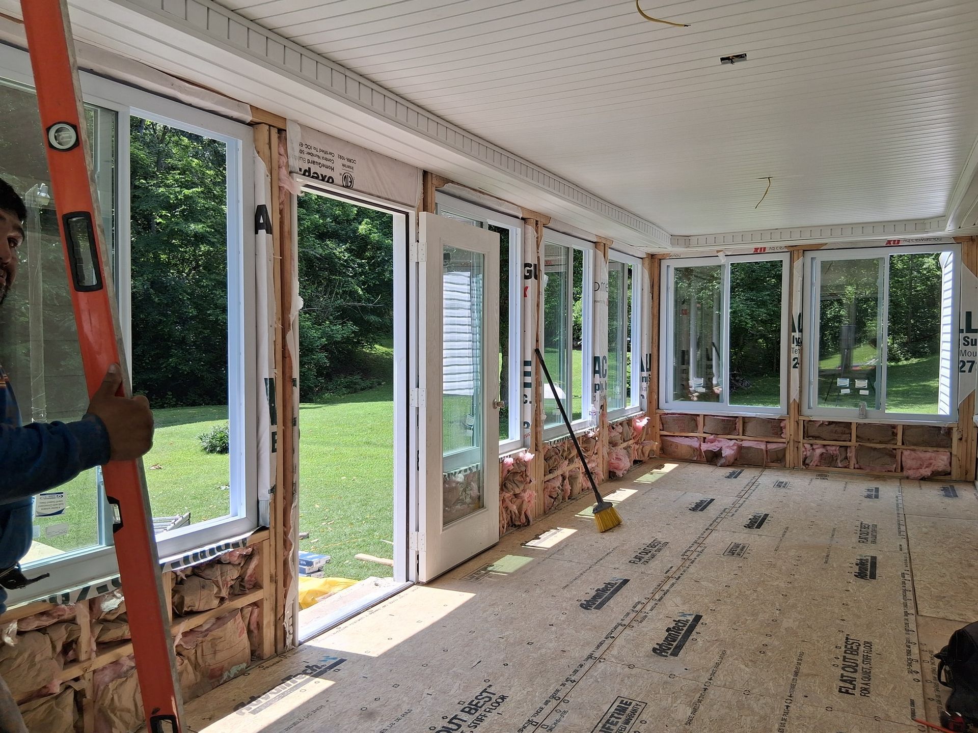 Man using level in room under construction with windows, door, and exposed insulation.