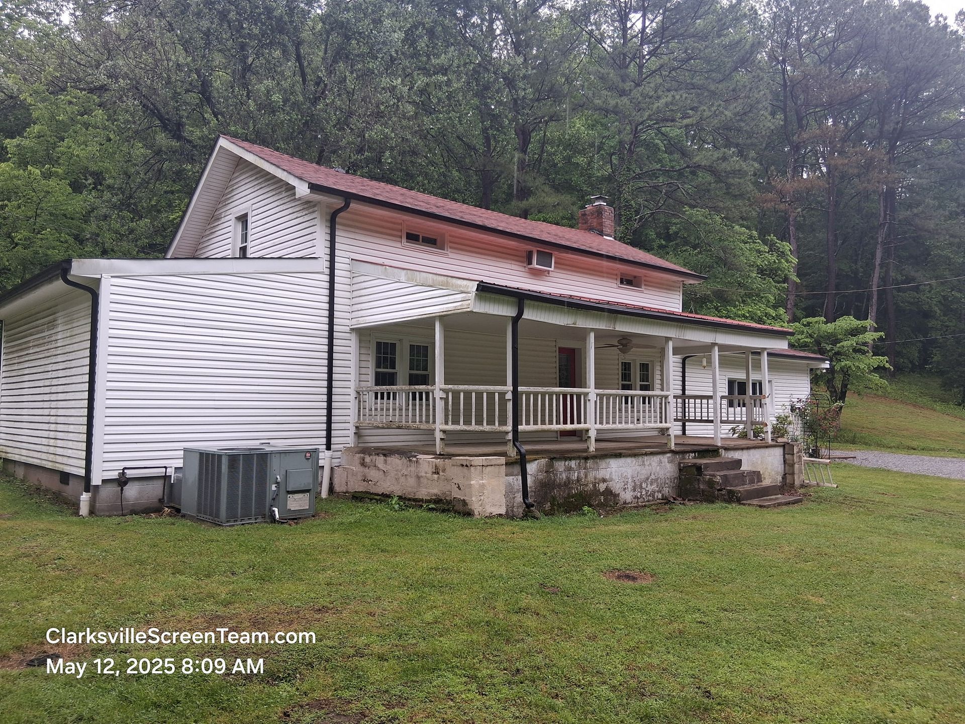 White house with porch, set in grassy yard, under a cloudy sky.