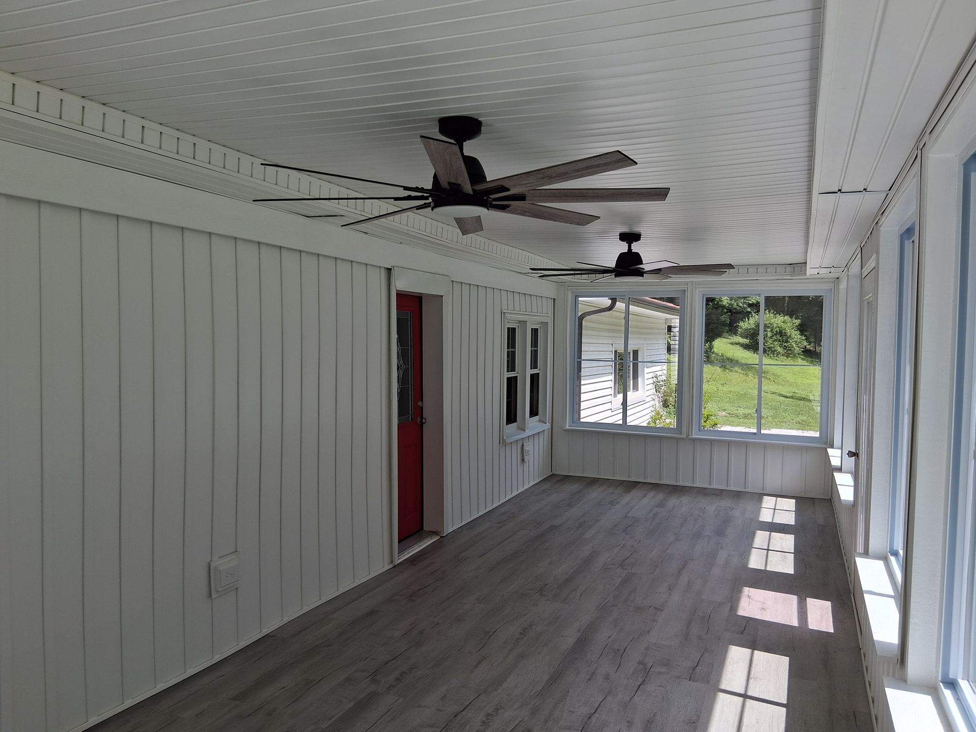 Bright sunroom with gray flooring, white walls, and two ceiling fans.