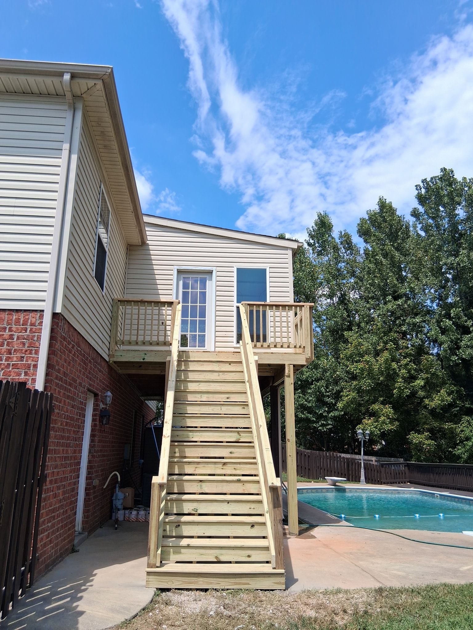 Wooden staircase leading up to a deck attached to a two-story building near a pool. Sunny, blue sky.
