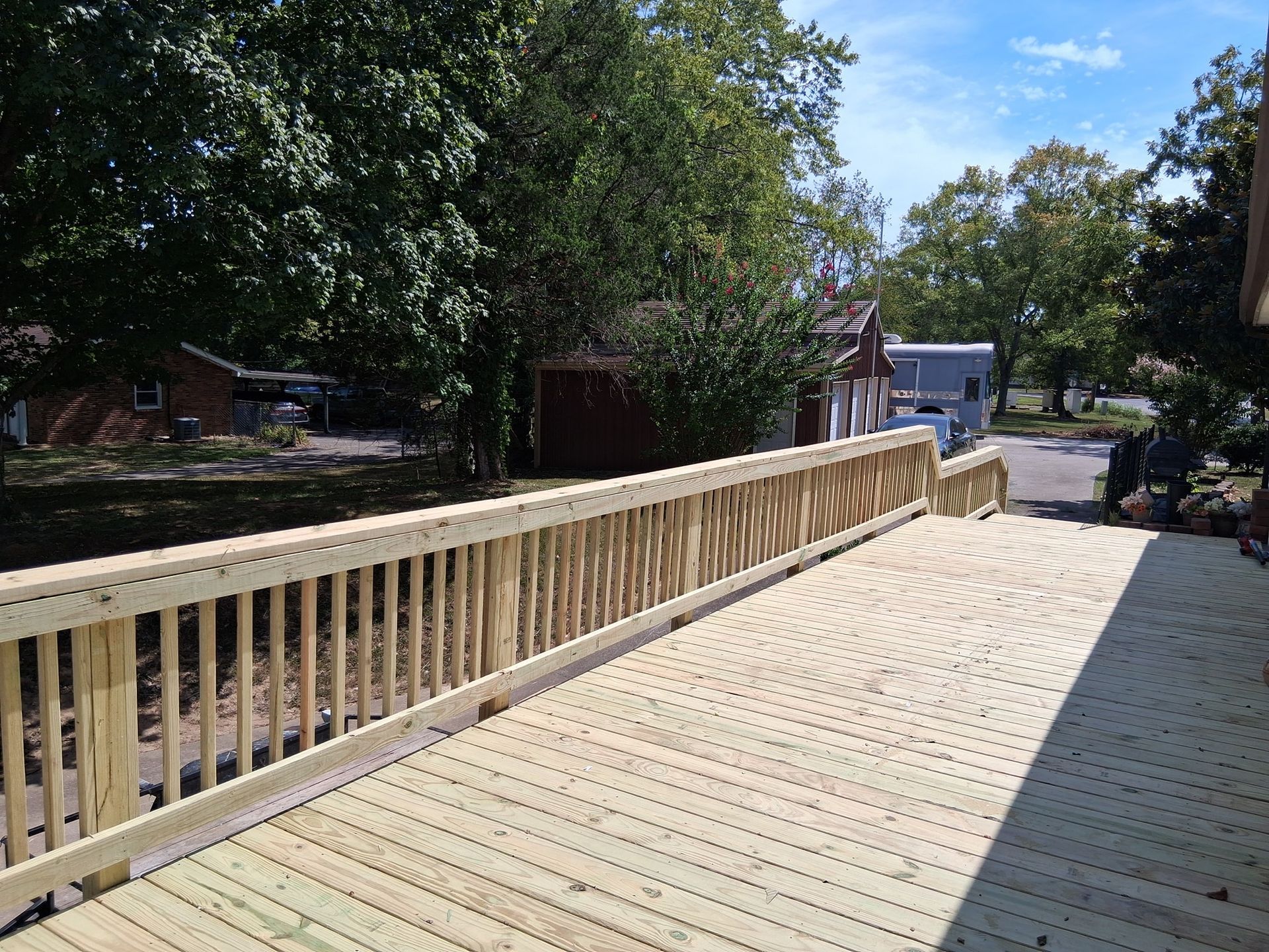 New wooden deck with railing; trees and buildings in background.