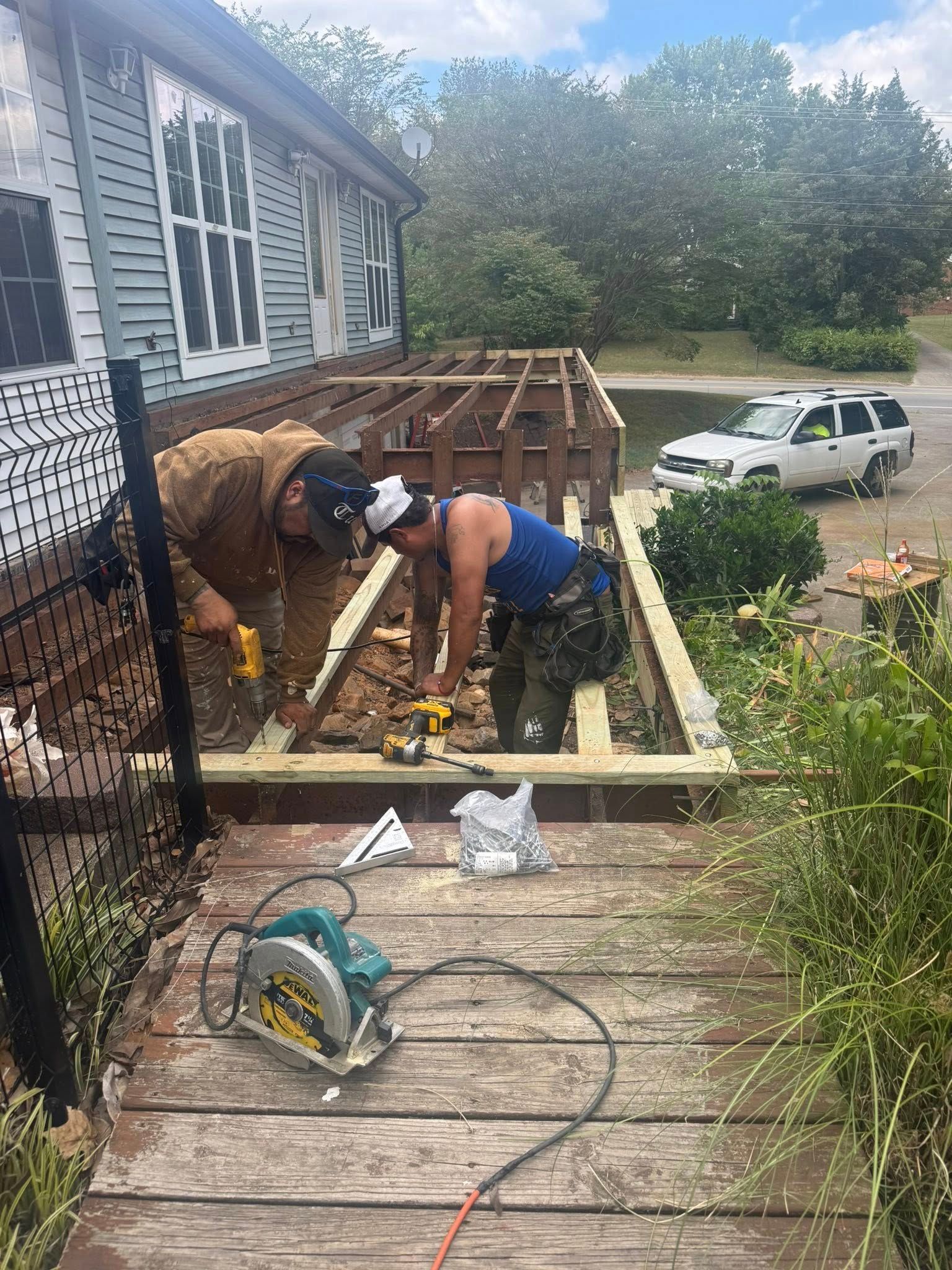 Two workers rebuilding a deck on a house, using power tools.