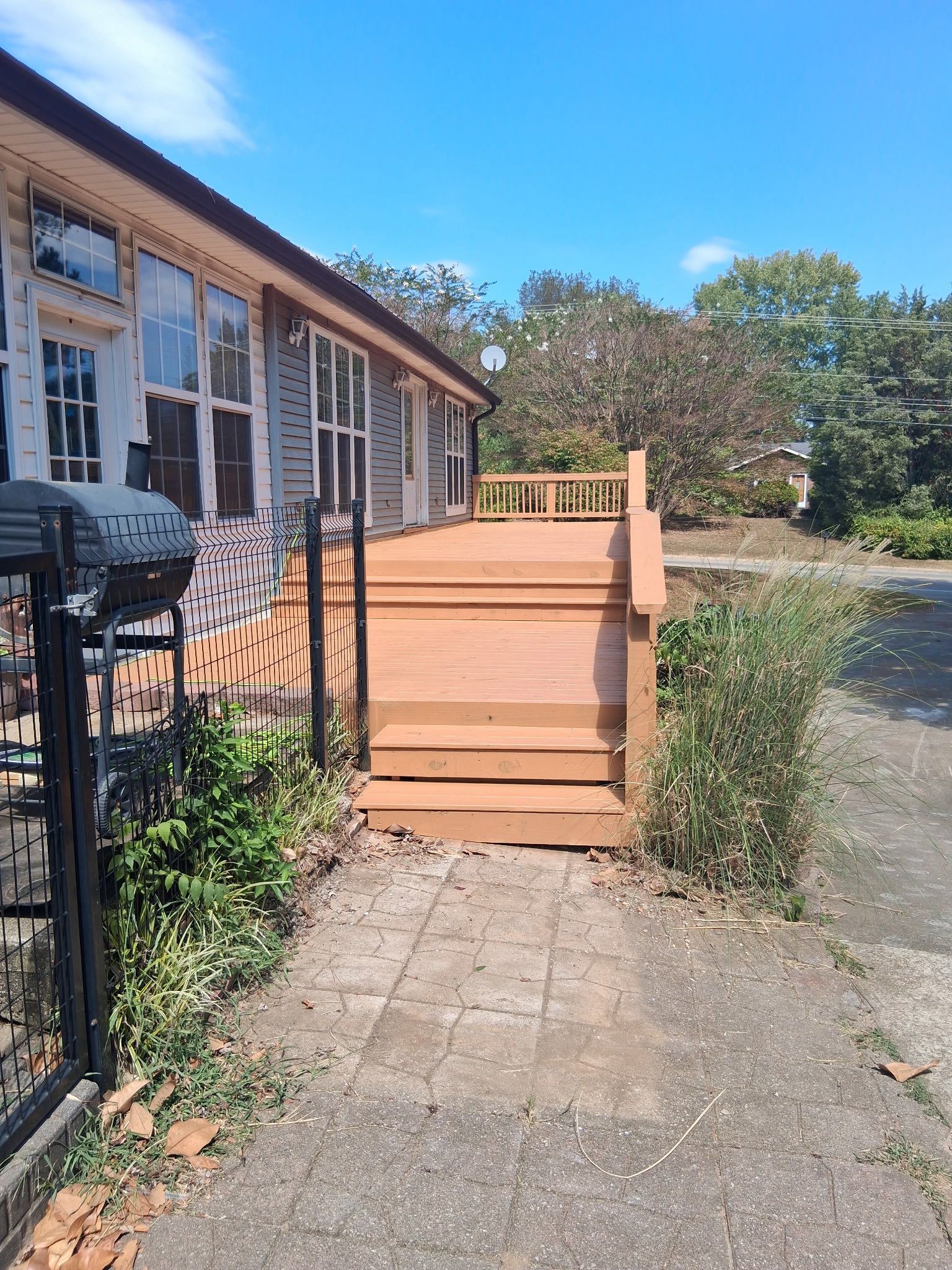Wooden deck with steps next to a house with large windows.