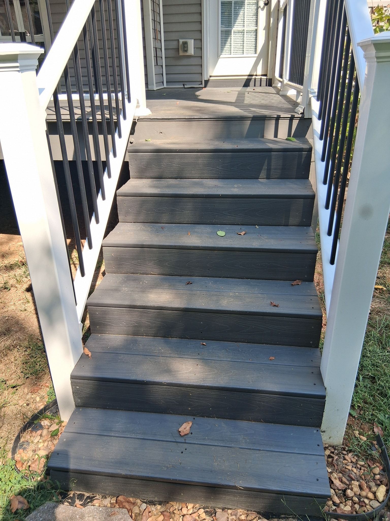 Outdoor wooden steps leading up to a porch, with black treads, white railing posts, and black railings.