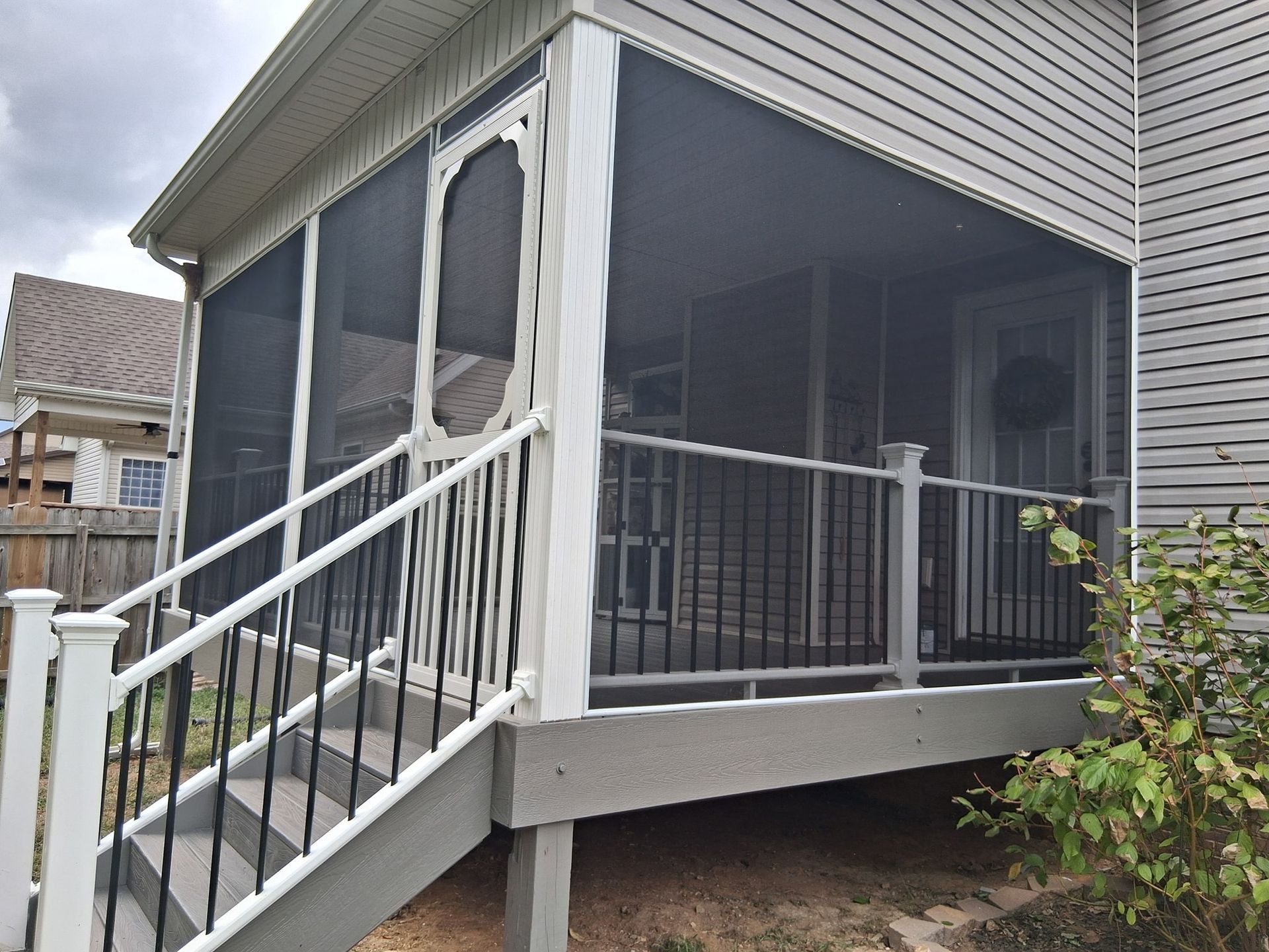 Screened-in porch with gray deck and siding, black railing, white trim, and staircase.