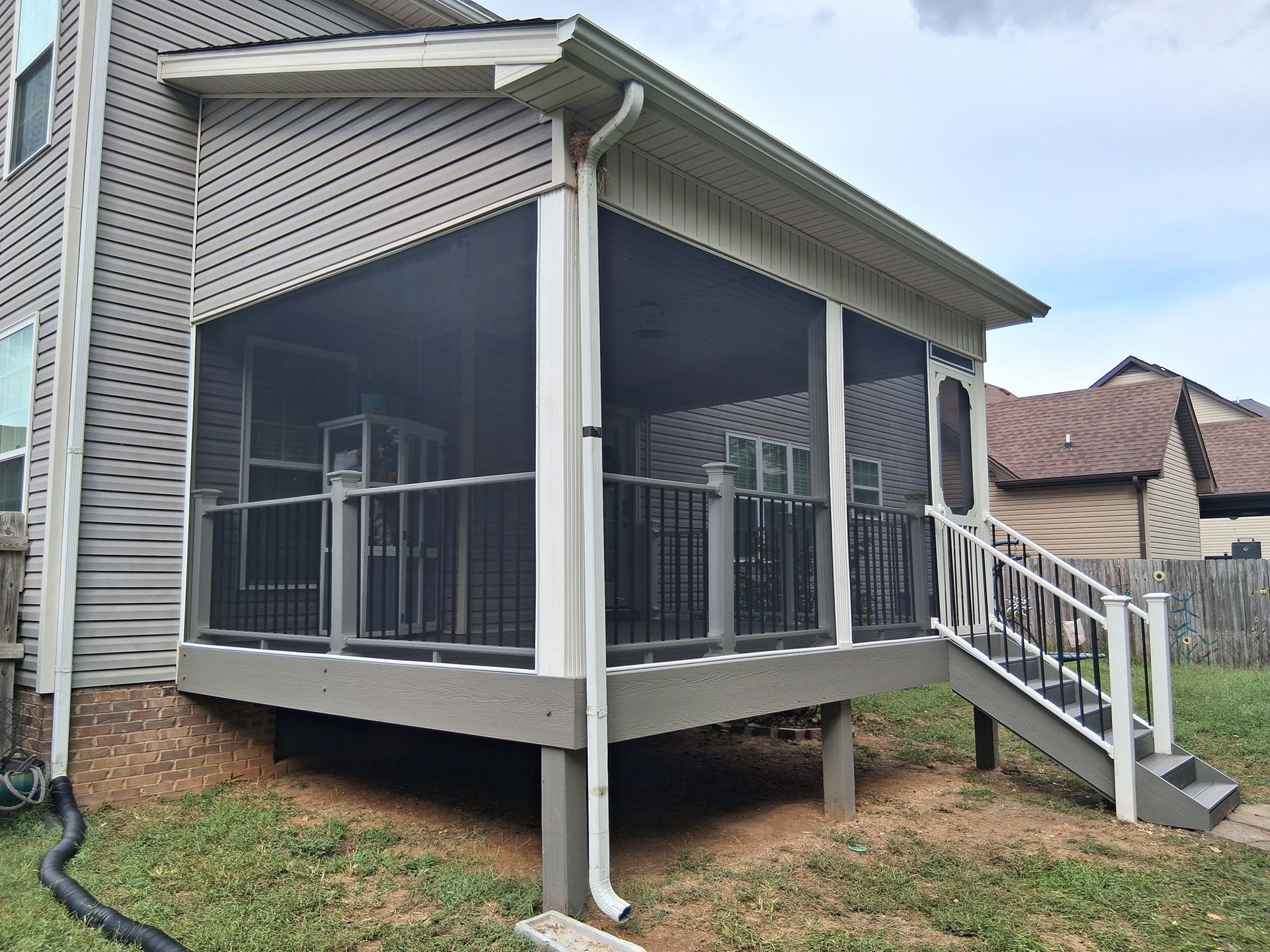Screened porch attached to a house with black railings, gray siding, and a white staircase.